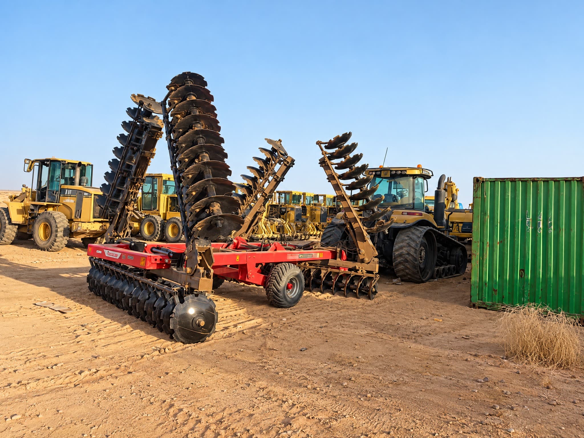 Folding disc harrows, tracked tractors, motor graders and a loader in the equipment yard.